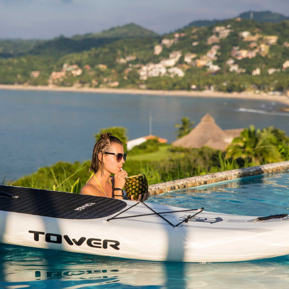 Woman drinking from a pineapple with a Tower paddle board next to her